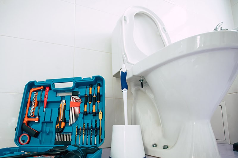 How to Unclog Your Slow-Draining Toilet in Boone. Close up photo of ceramic bowl toilet in domestic bathroom with a box of tools.